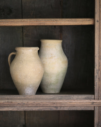 Two pale beige ceramic pitcher jars on a antique elm wooden shelf