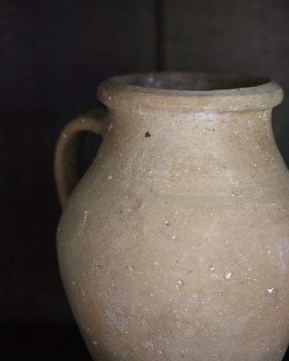 Close up of rustic textured clay vessel with a handle on a dark background