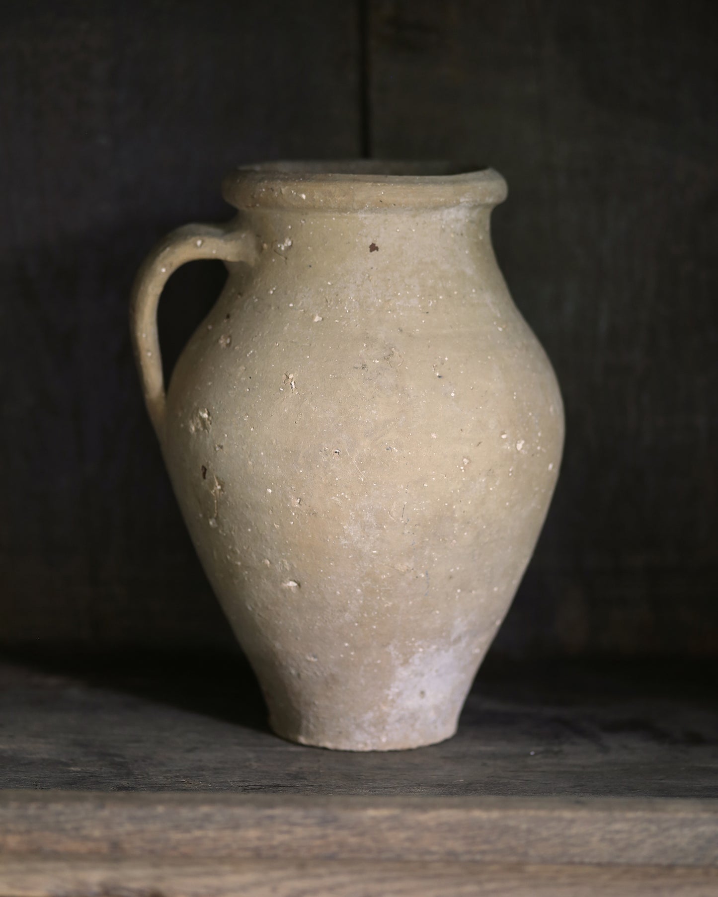 Beige ceramic vase on a dark wooden surface with a dark background