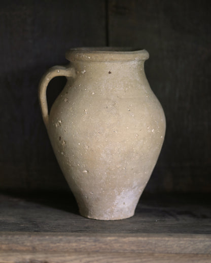 Beige ceramic vase on a dark wooden surface with a dark background