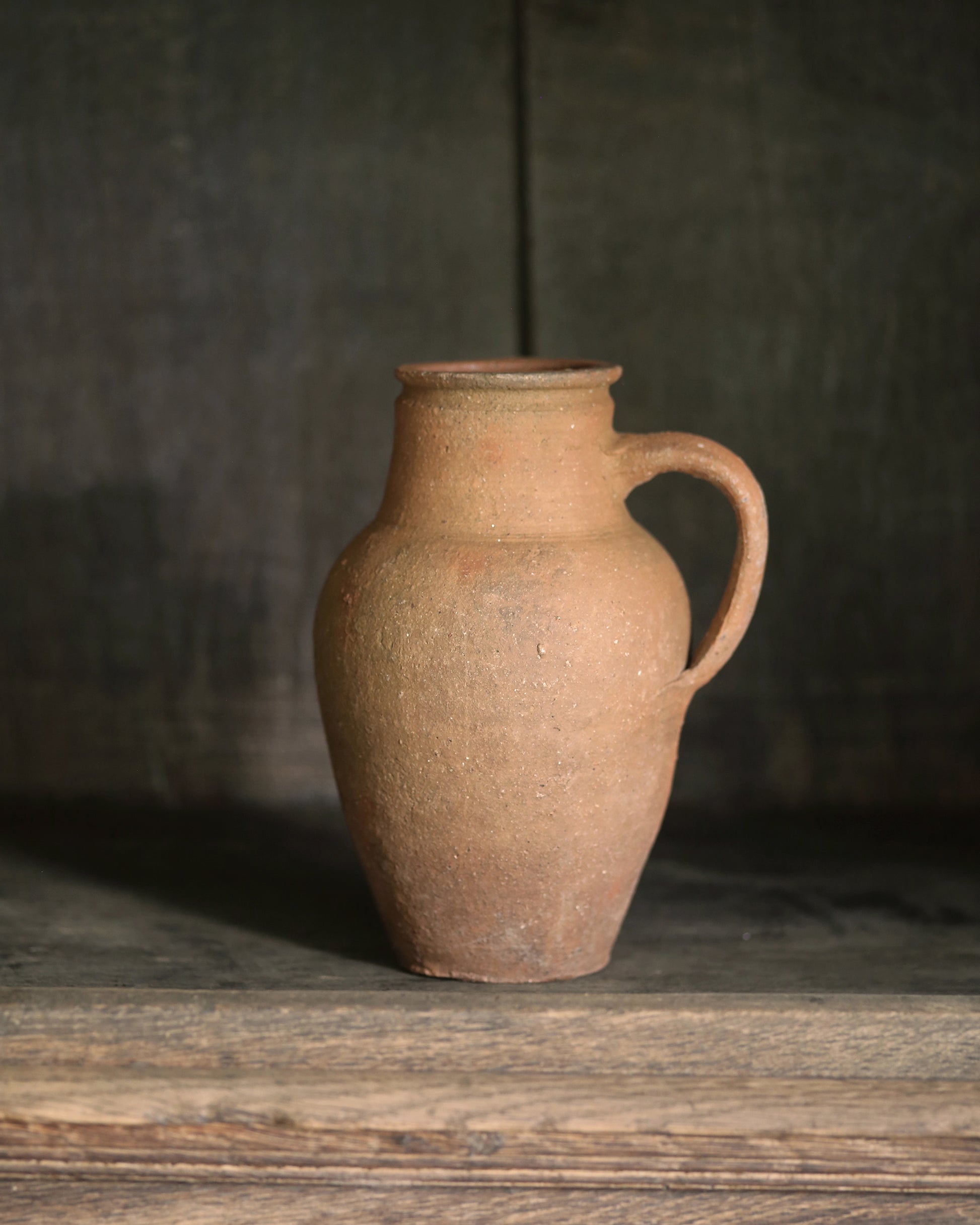 Brown ceramic jug on a wooden surface with a dark background