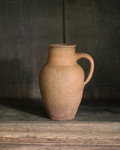 Brown ceramic jug on a wooden surface with a dark background