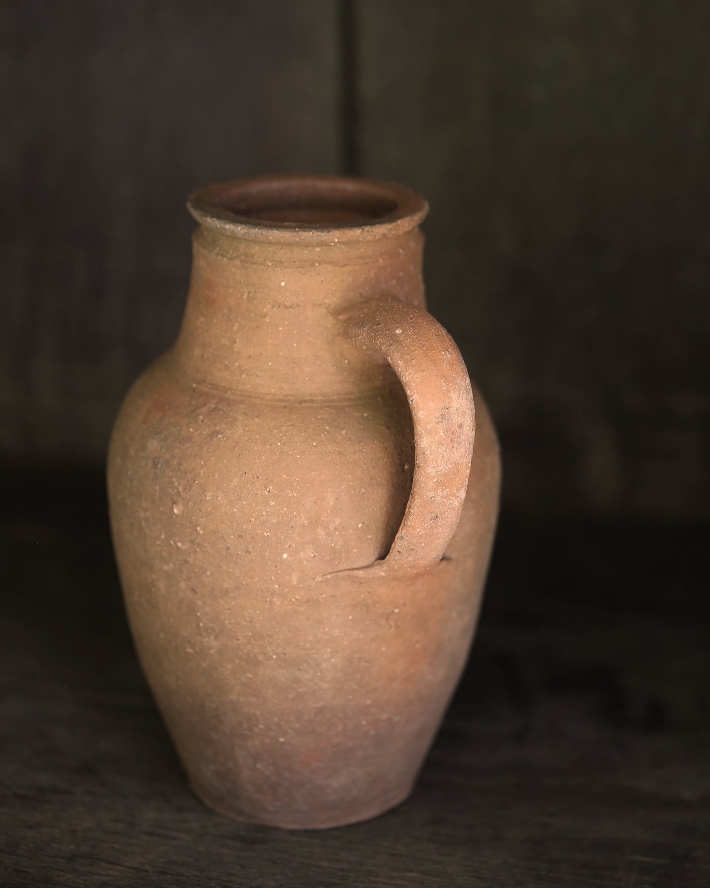 Brown ceramic jar with a handle on a dark background