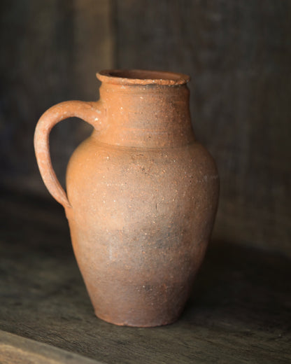Brown clay vintage pitcher pot on a dark surface with a blurred background