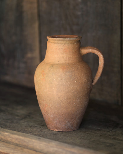 Terracotta pitcher on a wooden surface with a blurred background