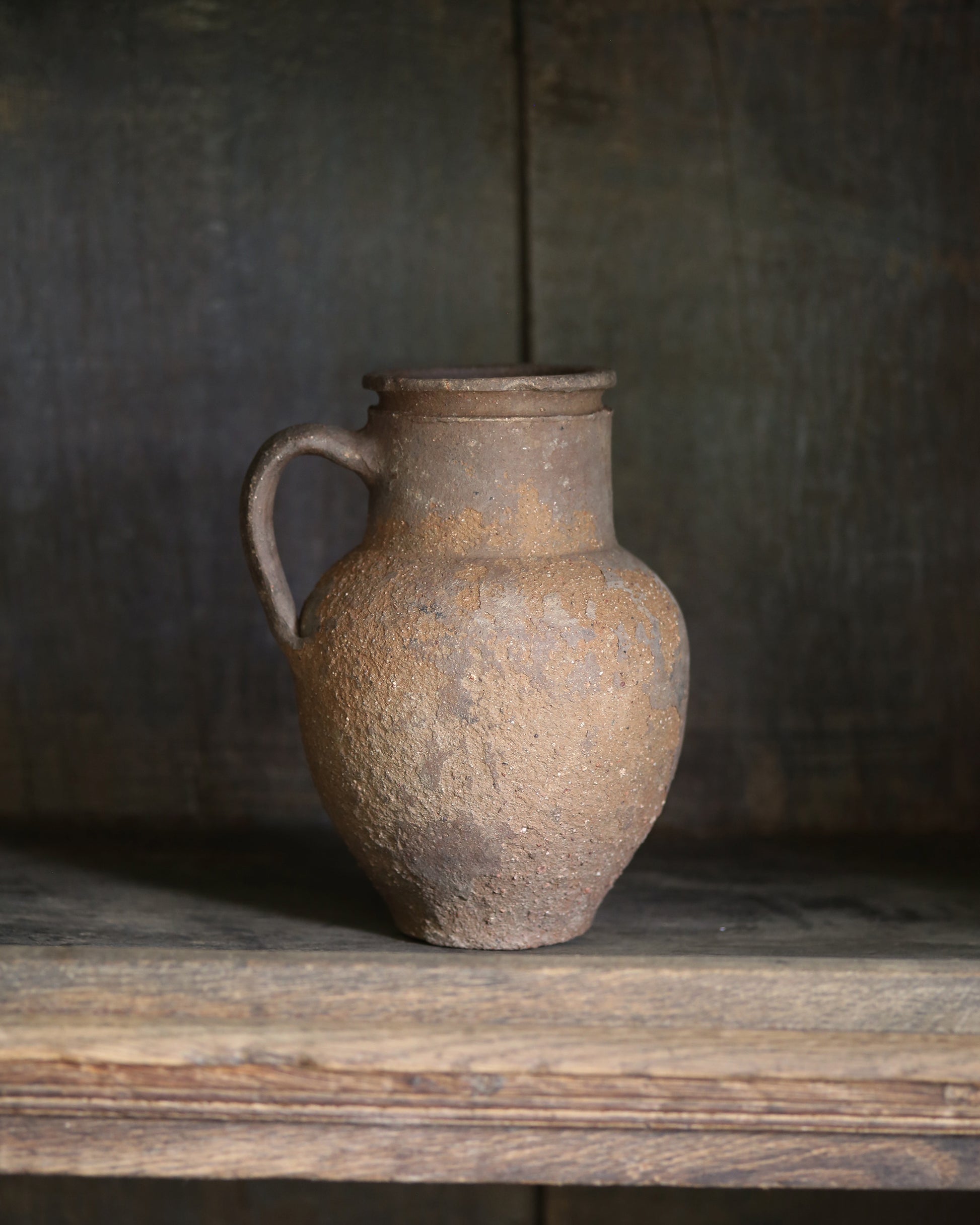 Vintage terracotta pitcher pot on a wooden surface with a dark background