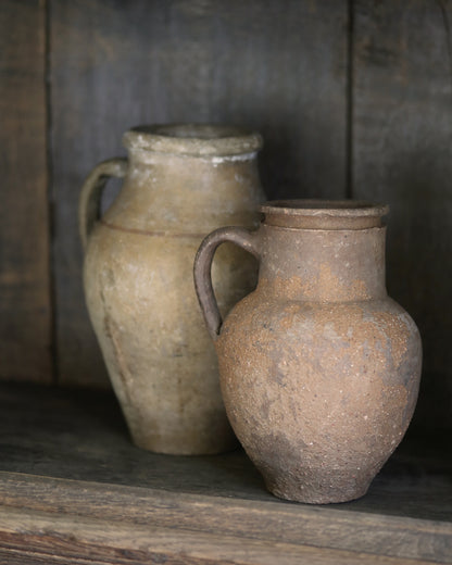 Two rustic clay handled pots on a wooden surface with a dark background