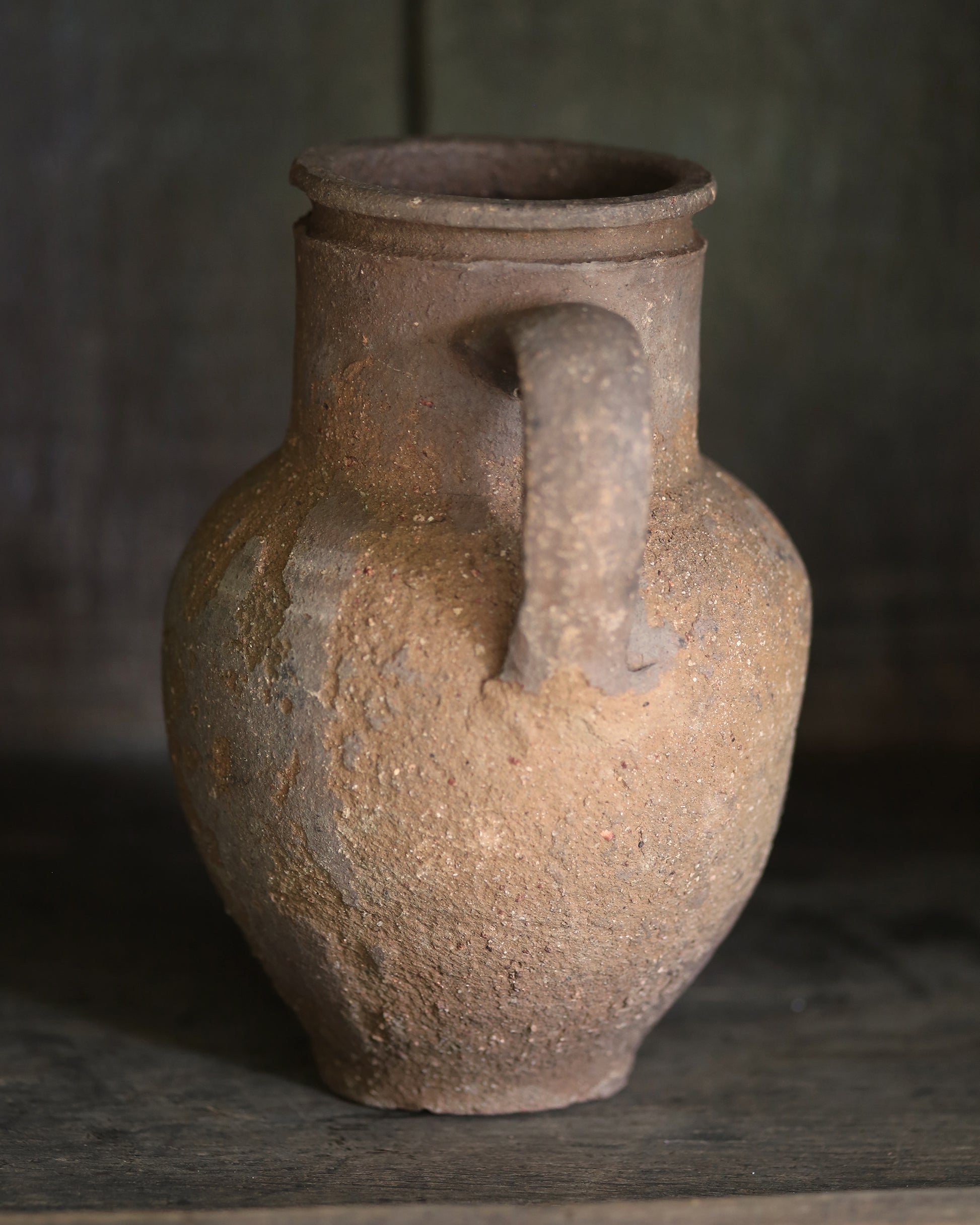 Brown rustic clay jar with a handle on a dark background