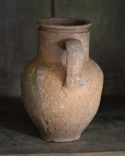 Brown rustic clay jar with a handle on a dark background
