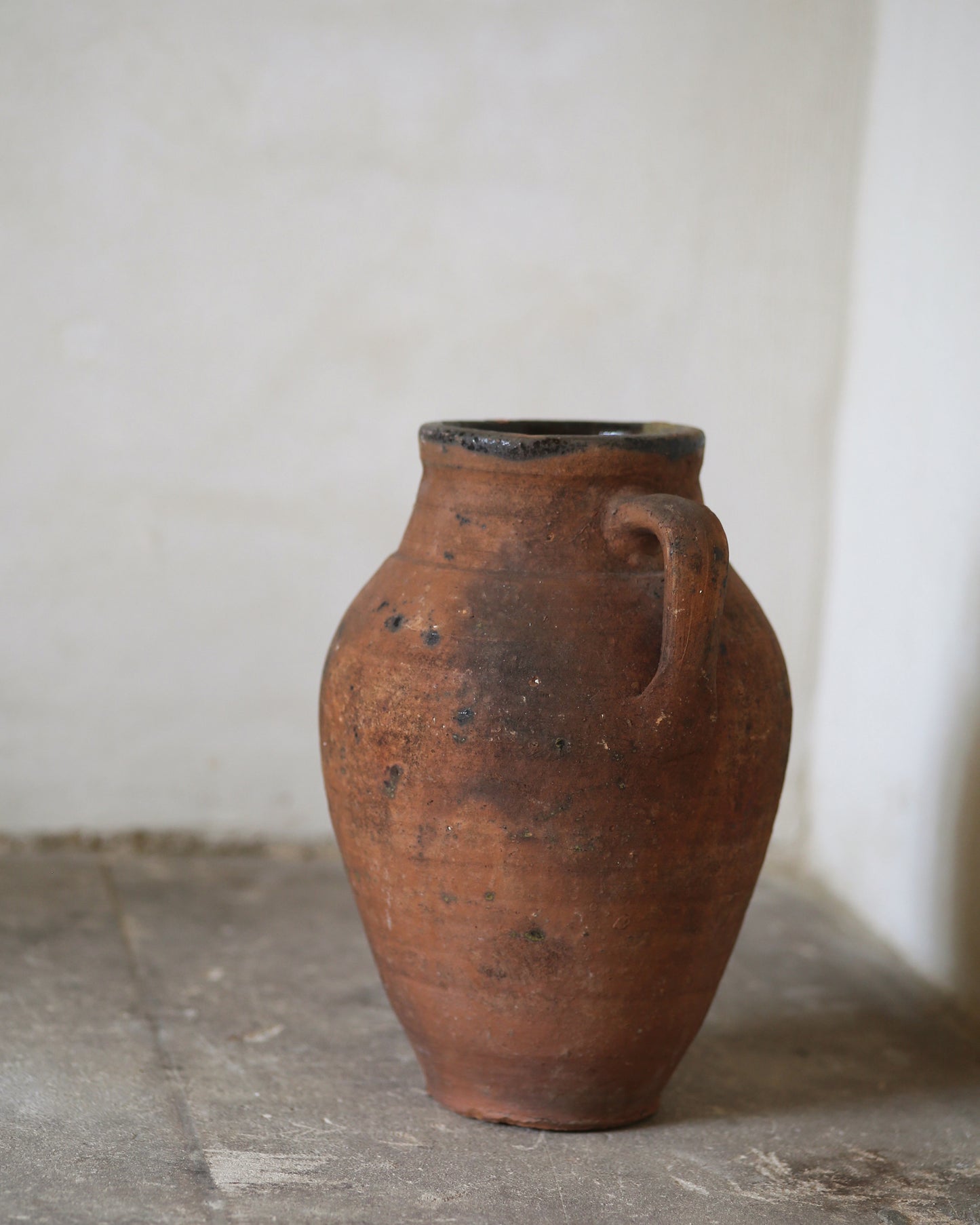 Terracotta vase with a handle on a stone floor against a white wall