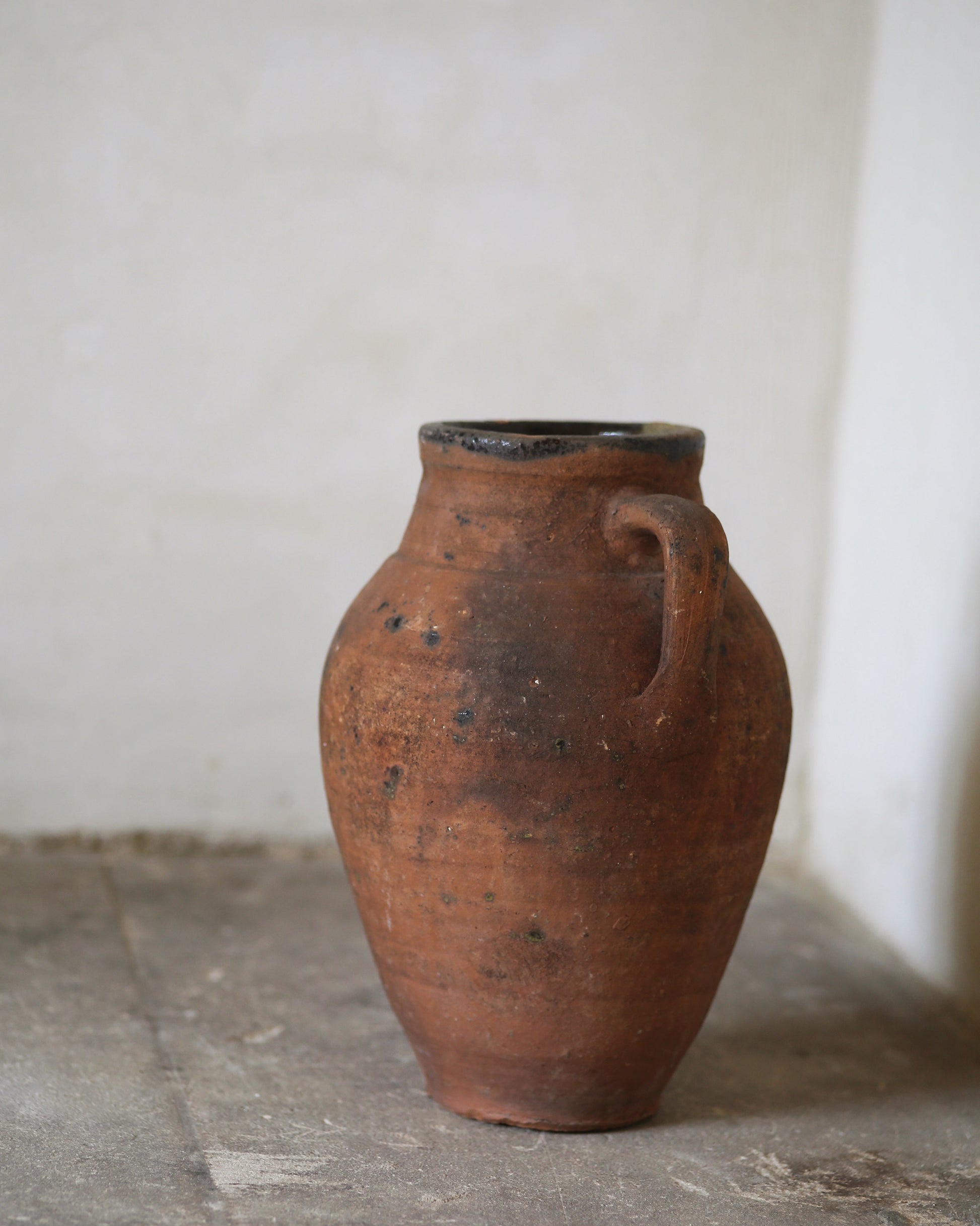 Terracotta vase with a handle on a stone floor against a white wall