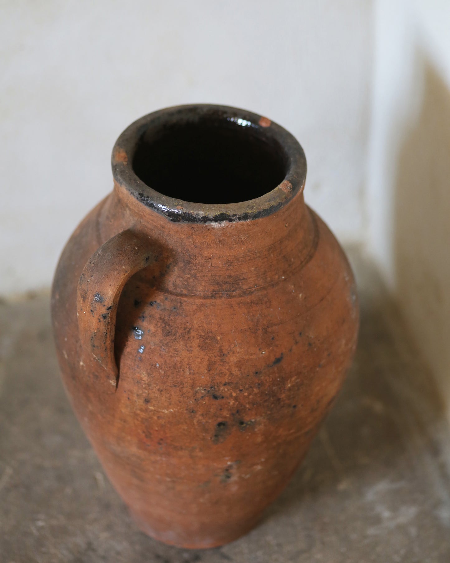 Terracotta vase with a single handle on a neutral background