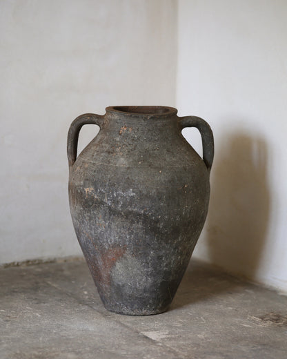 Vintage terracotta urn with handles on a concrete floor against a white wall