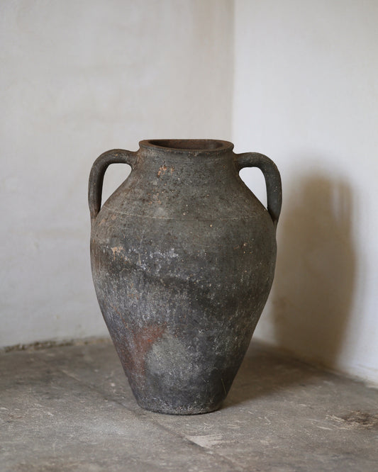 Vintage terracotta urn with handles on a concrete floor against a white wall