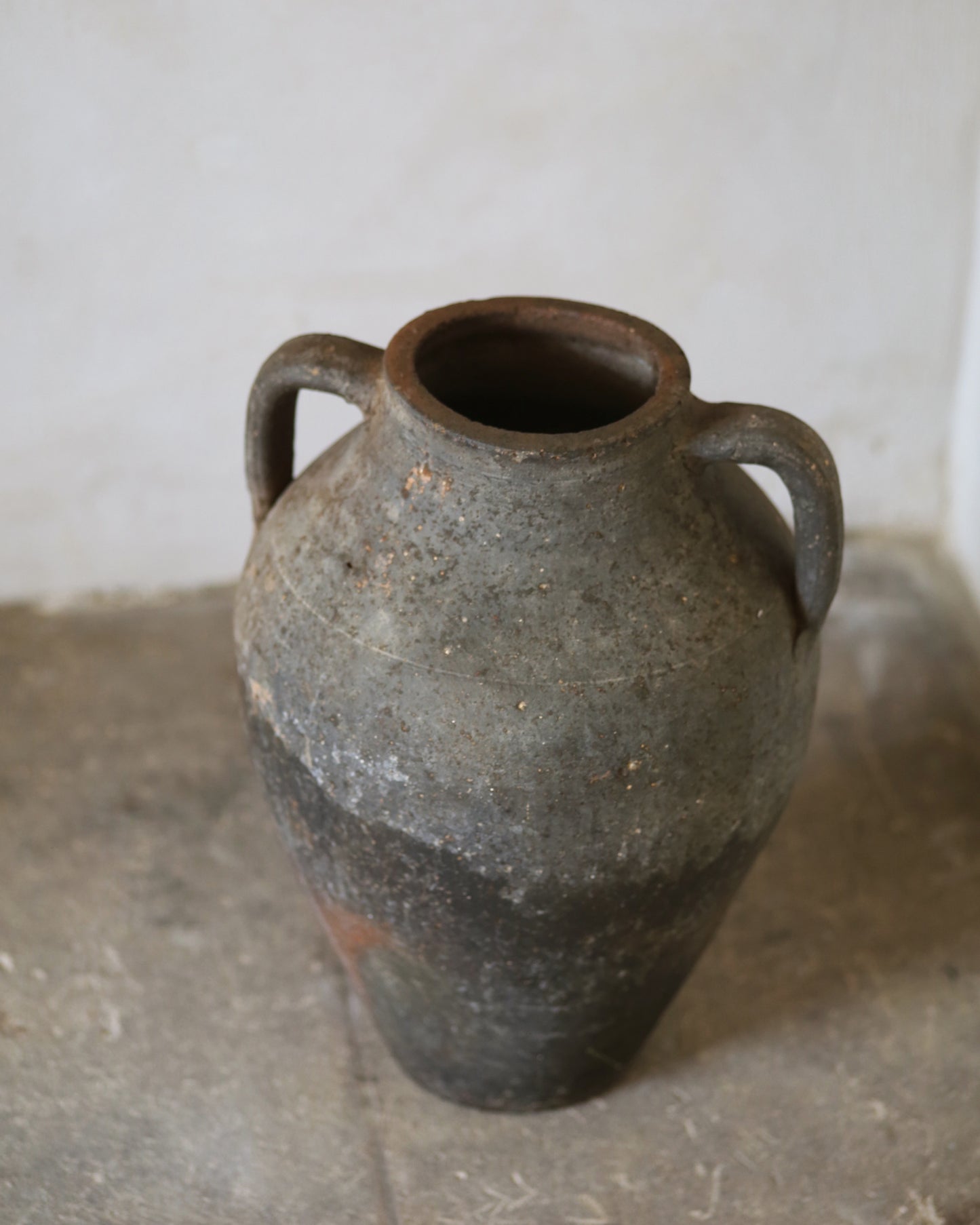 Vintage ceramic jar with two handles on a concrete floor.