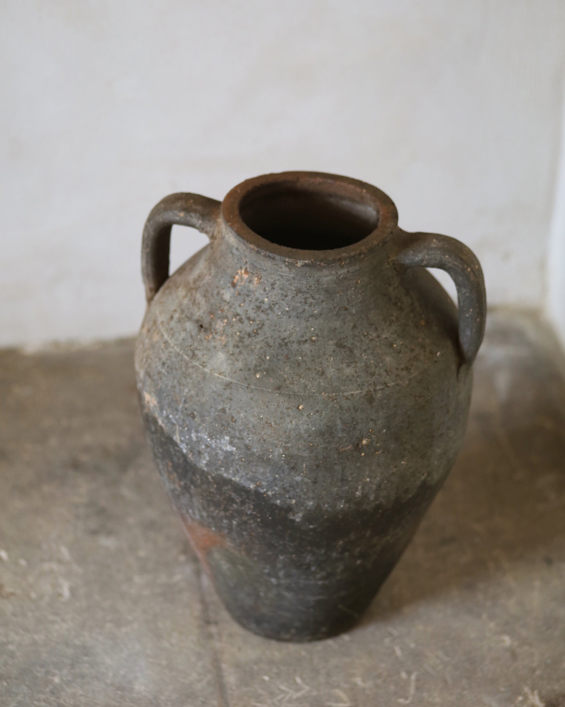 Vintage ceramic jar with two handles on a concrete floor.