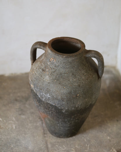 Vintage ceramic jar with two handles on a concrete floor.