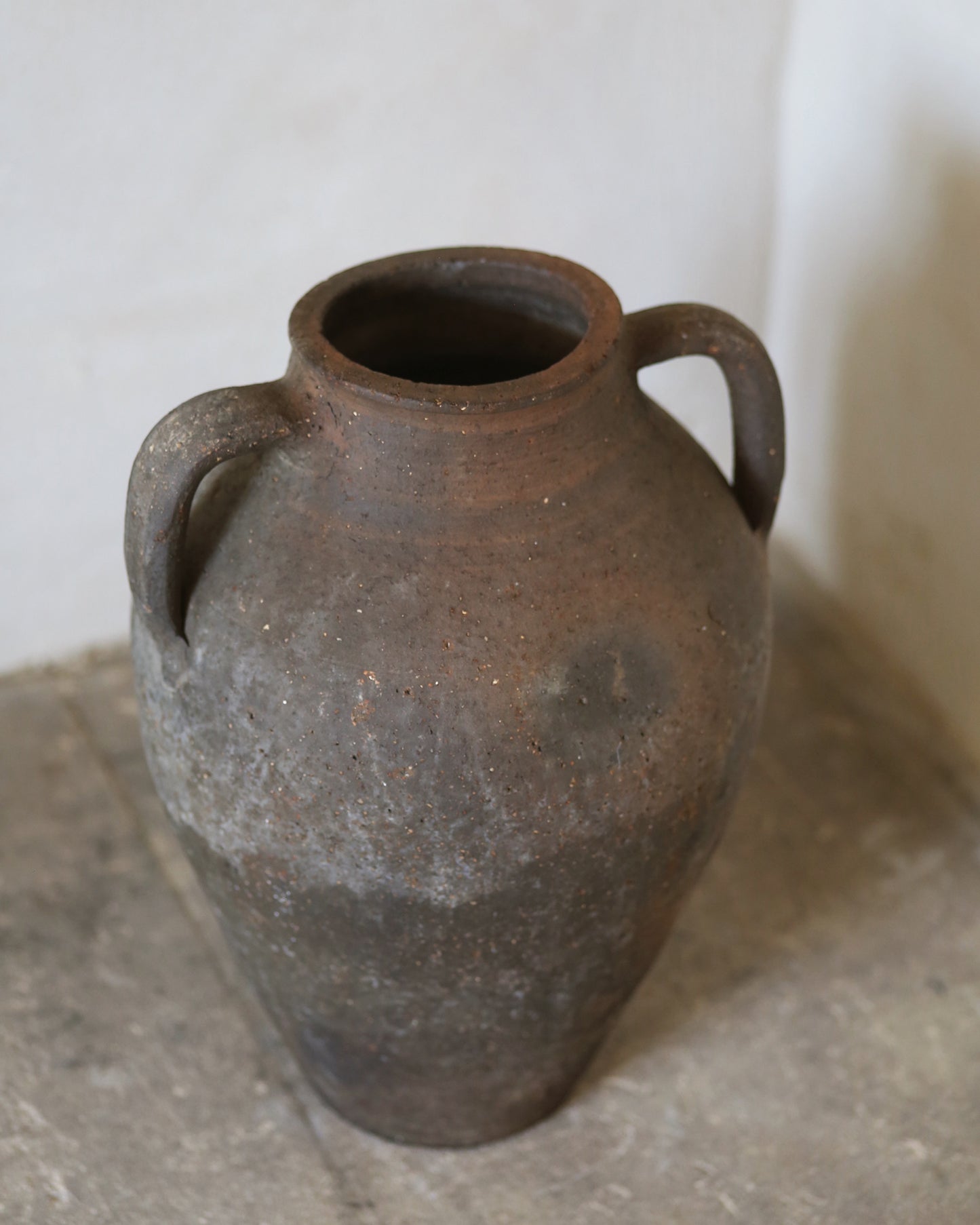Brown ceramic vase with two handles on a stone surface.
