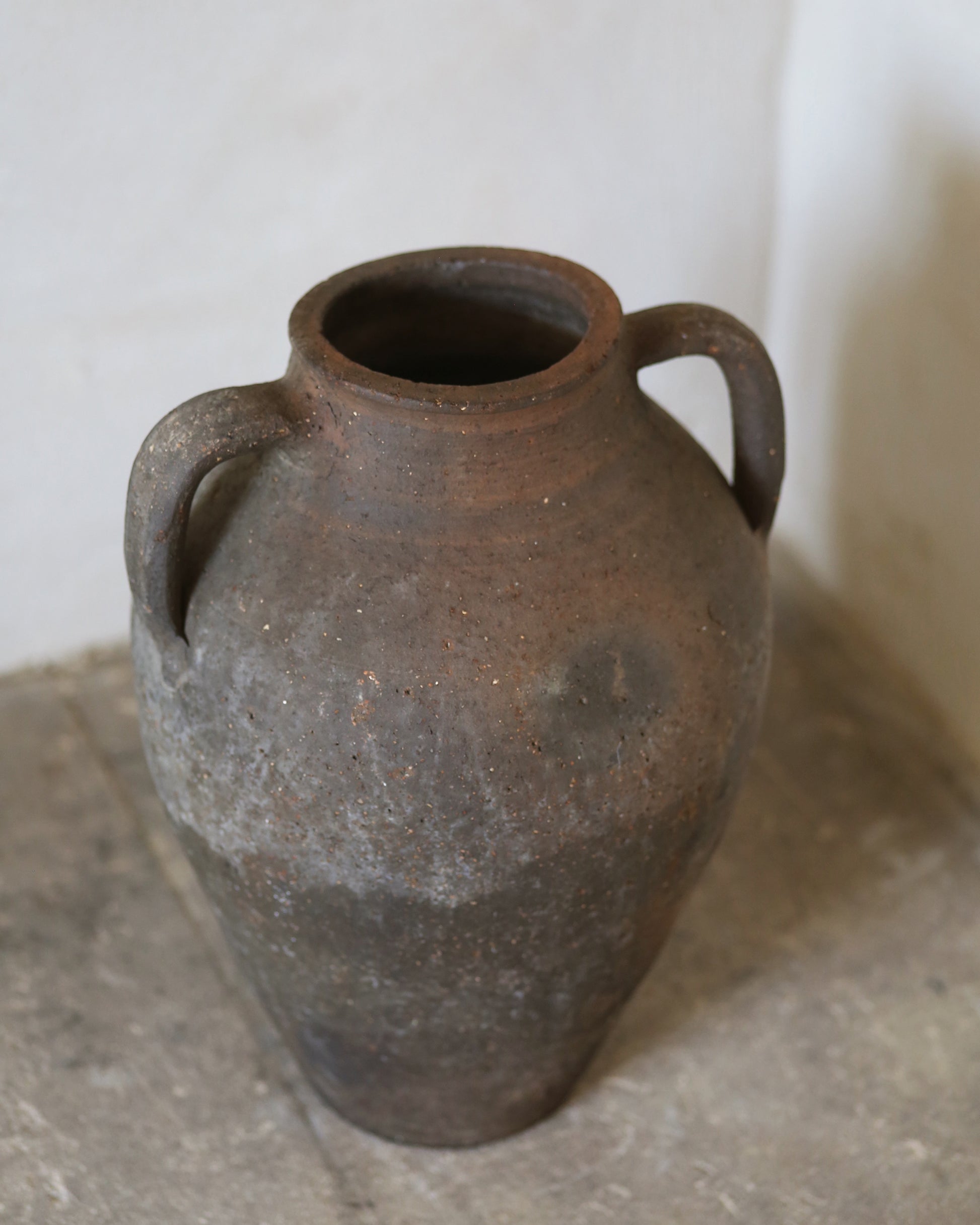 Brown ceramic vase with two handles on a stone surface.