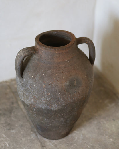 Brown ceramic vase with two handles on a stone surface.