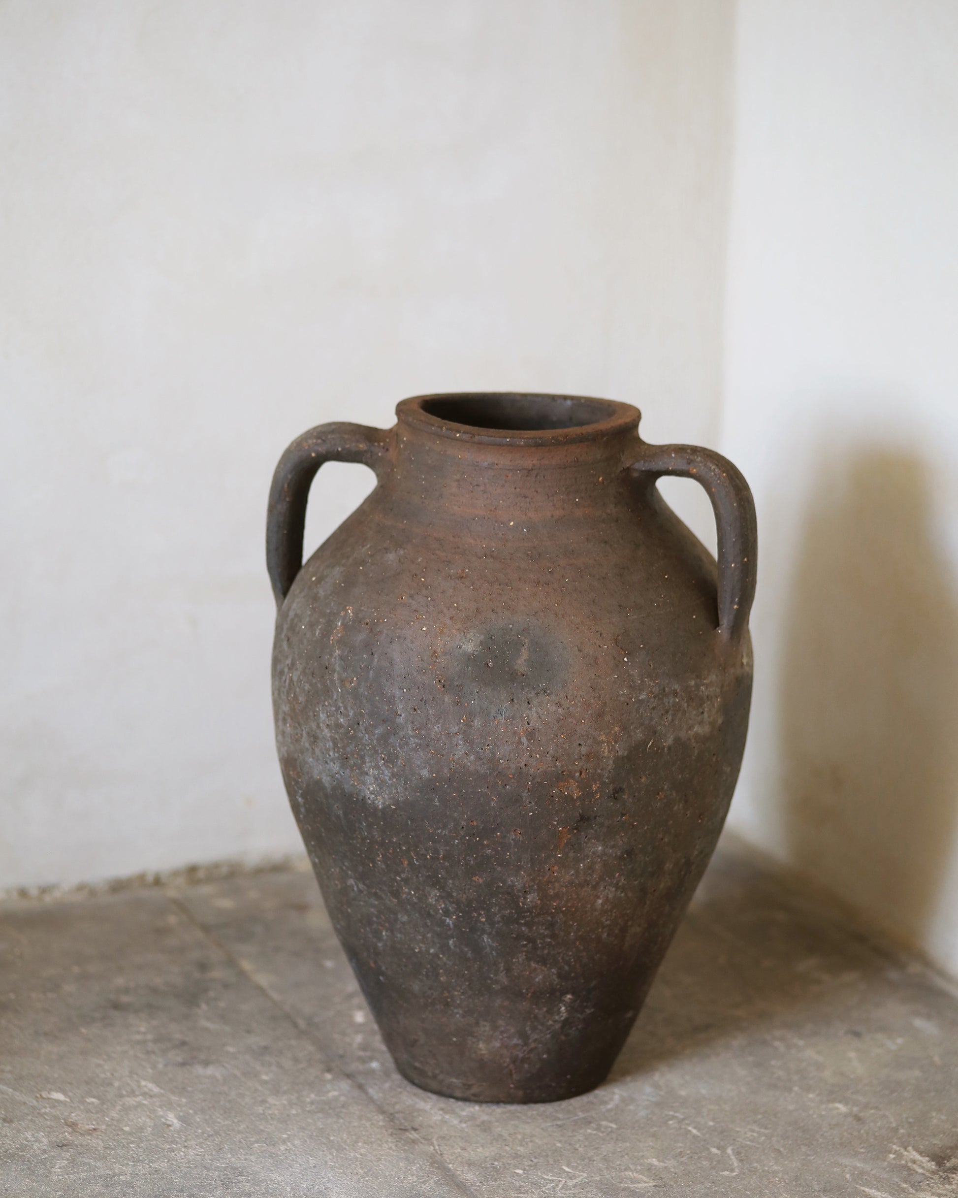 Vintage terracotta vase with handles on a stone surface against a white wall