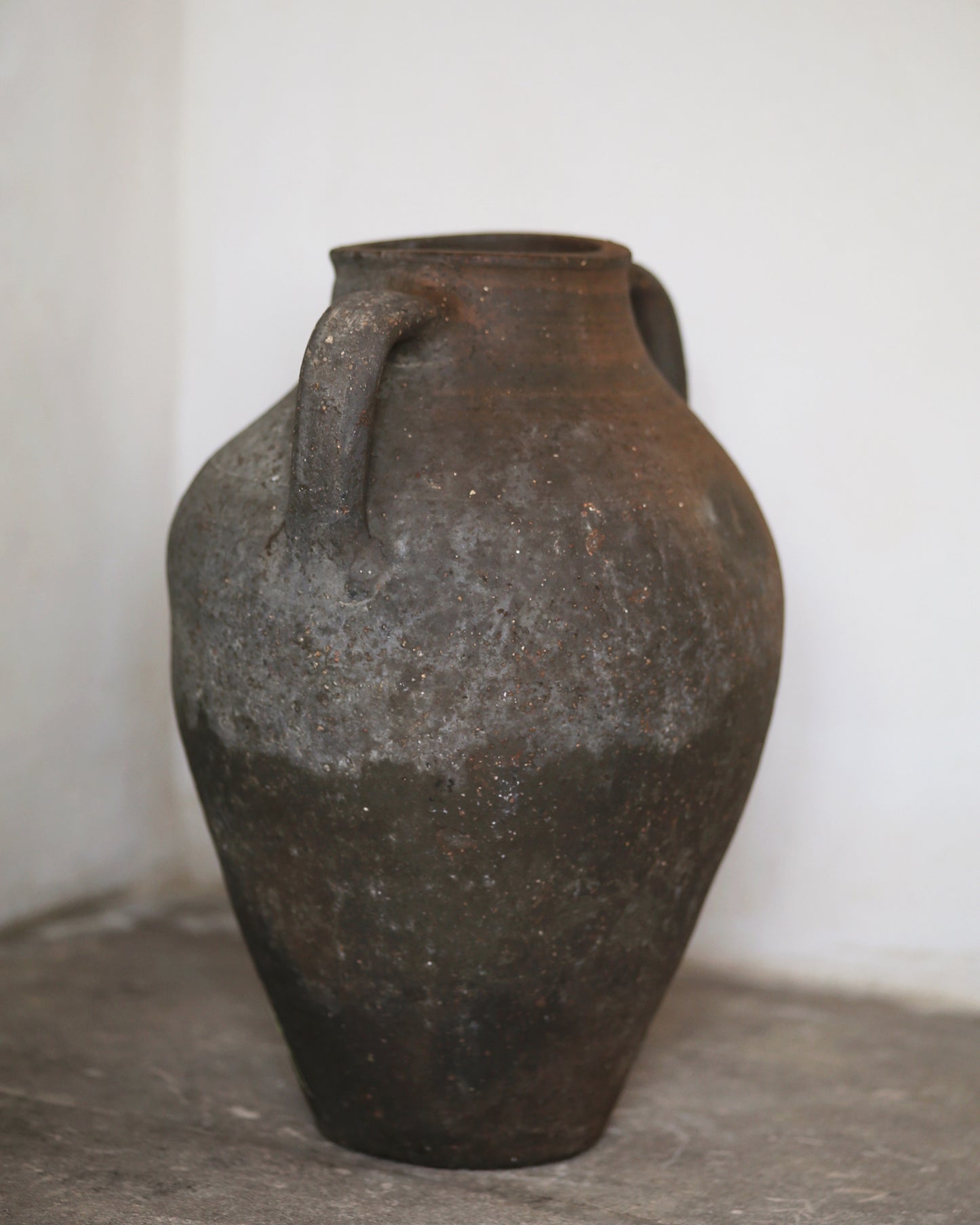 Vintage terracotta jar with two handles on a gray surface.