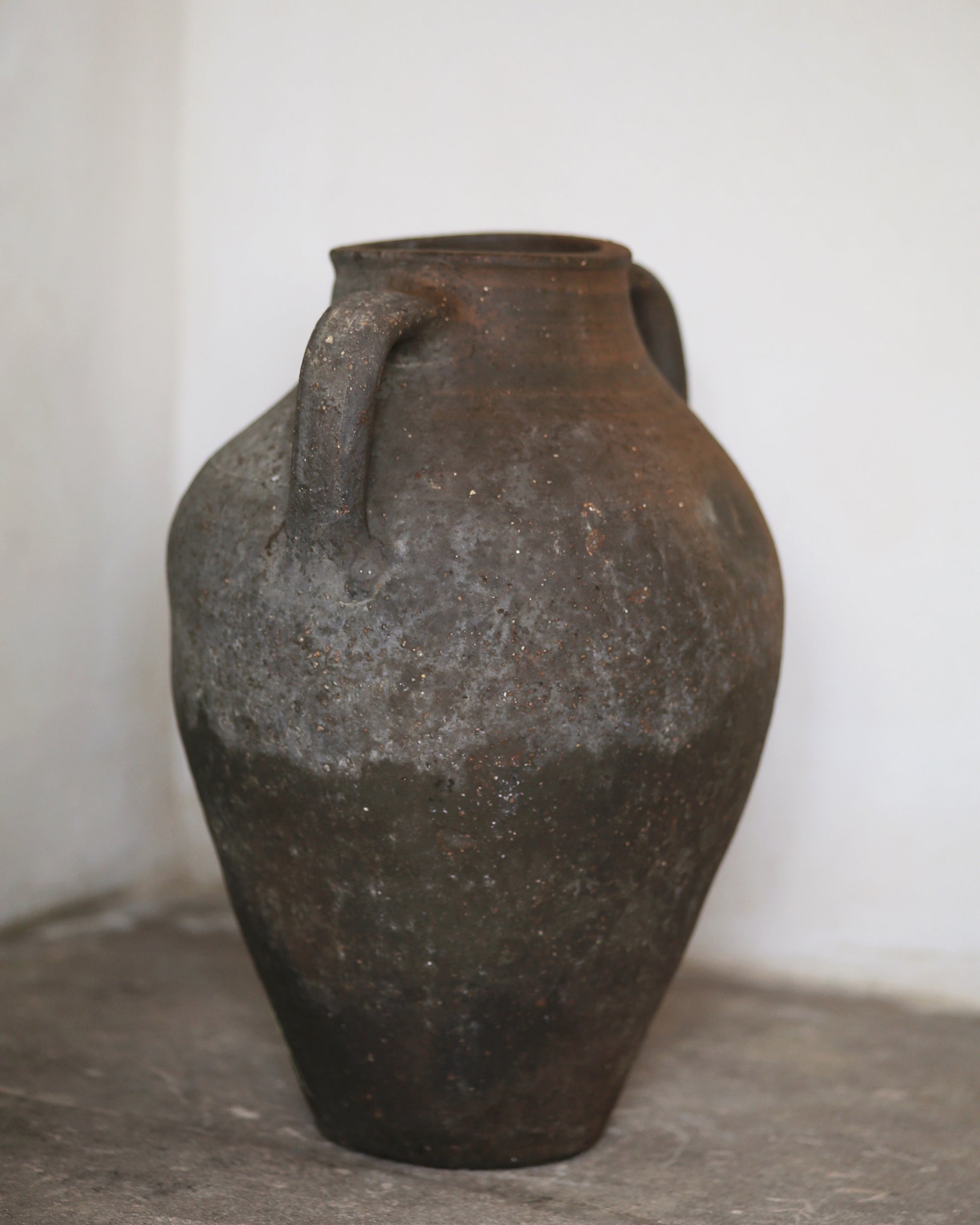Vintage terracotta jar with two handles on a gray surface.