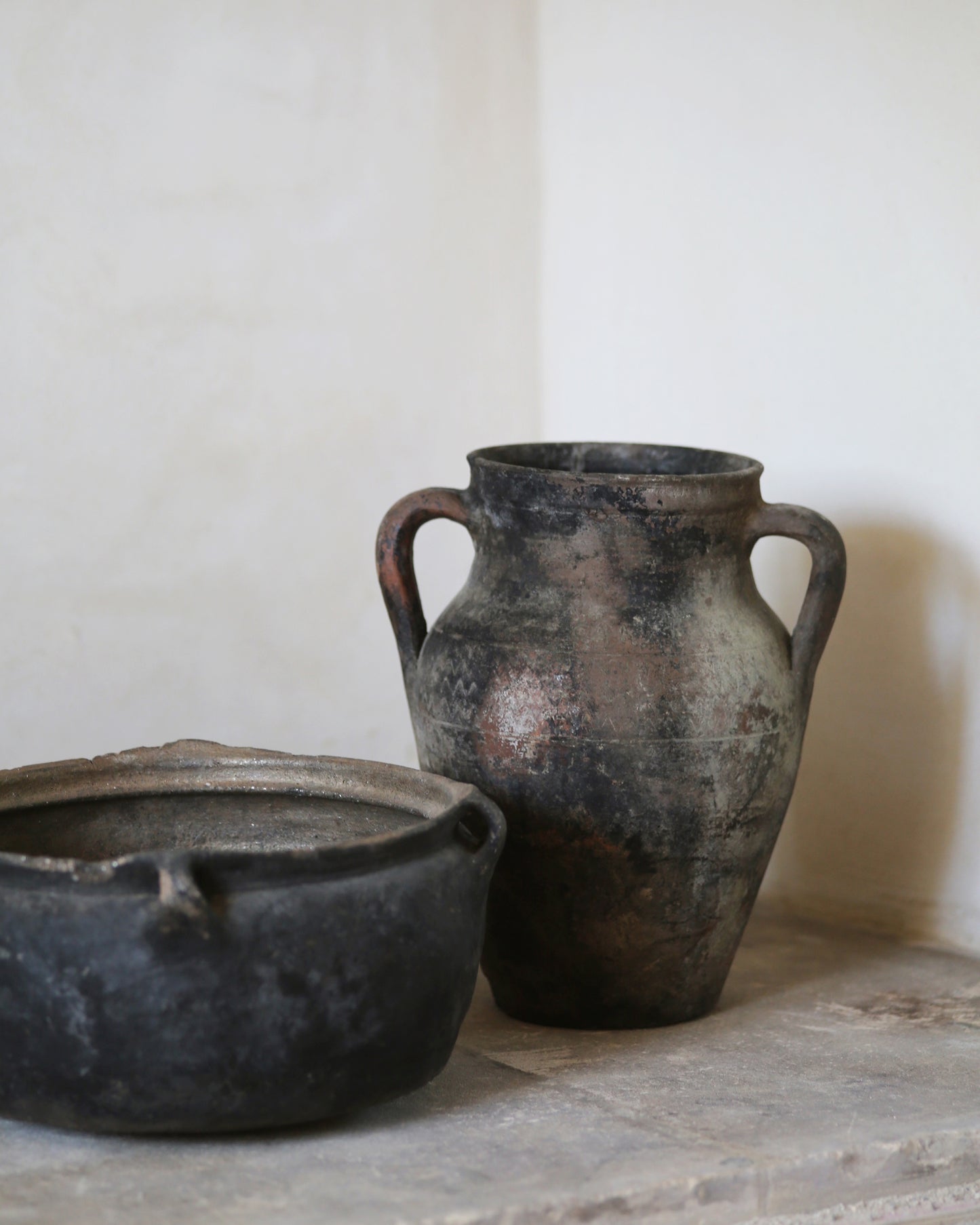 Two rustic black clay pots on a stone surface with a white background