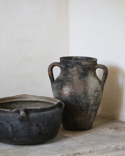 Two rustic black clay pots on a stone surface with a white background