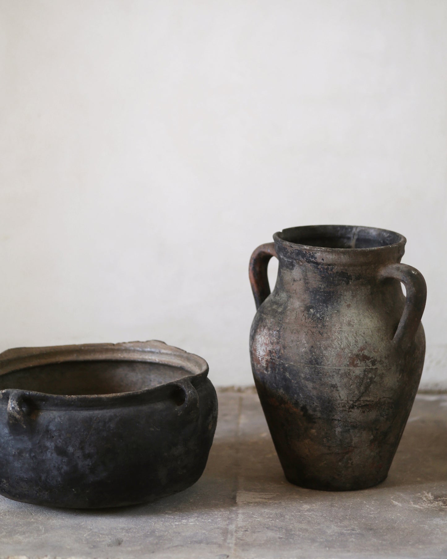 Two ancient-looking black pots on a stone surface with a white background