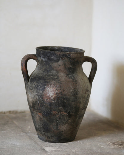 Ancient terracotta vase with two handles on a stone surface.