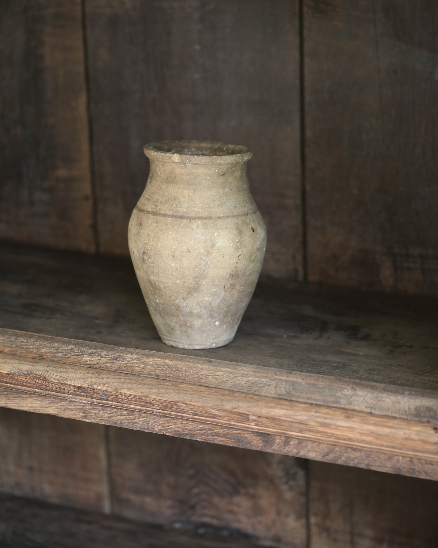 Vintage terracotta pot on a wooden shelf with a rustic wooden wall background