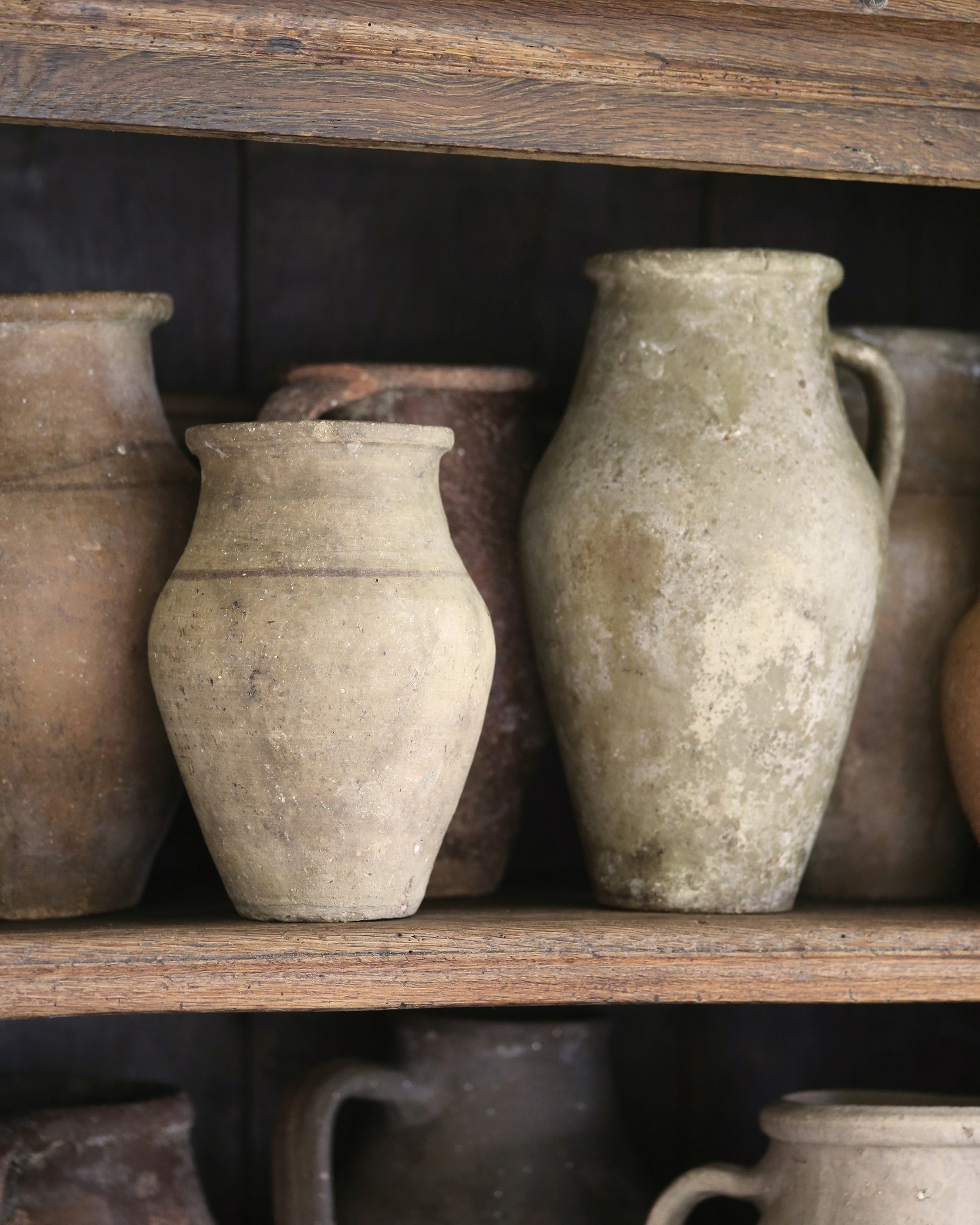 Collection of antique rustic clay pots styled on a wooden bookcase