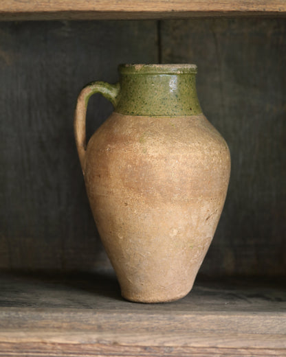 Stoneware pitcher with green rim on a wooden shelf