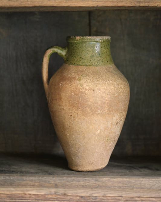 Stoneware pitcher with green rim on a wooden shelf