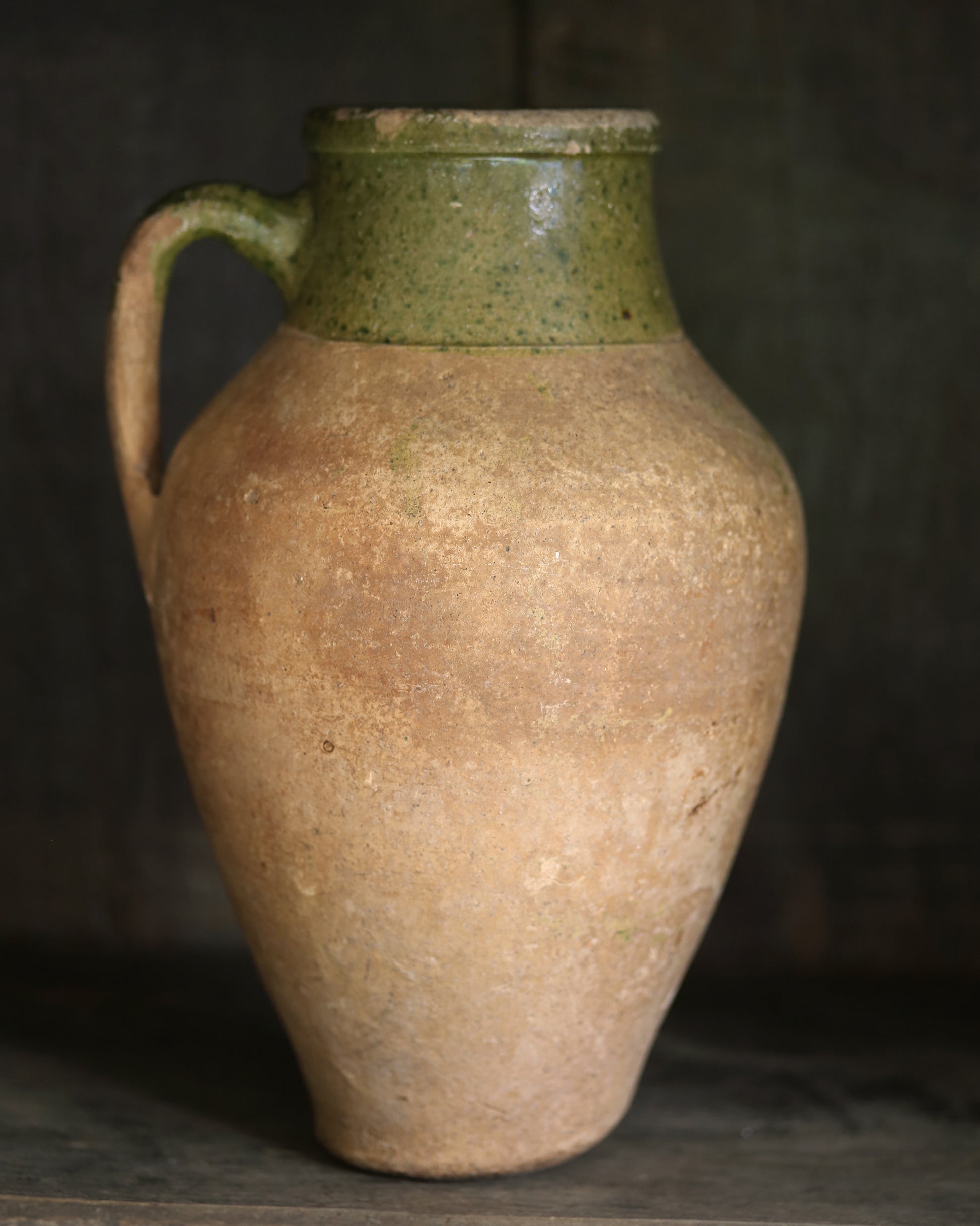 Vintage ceramic jar with a green glaze rim on a dark background