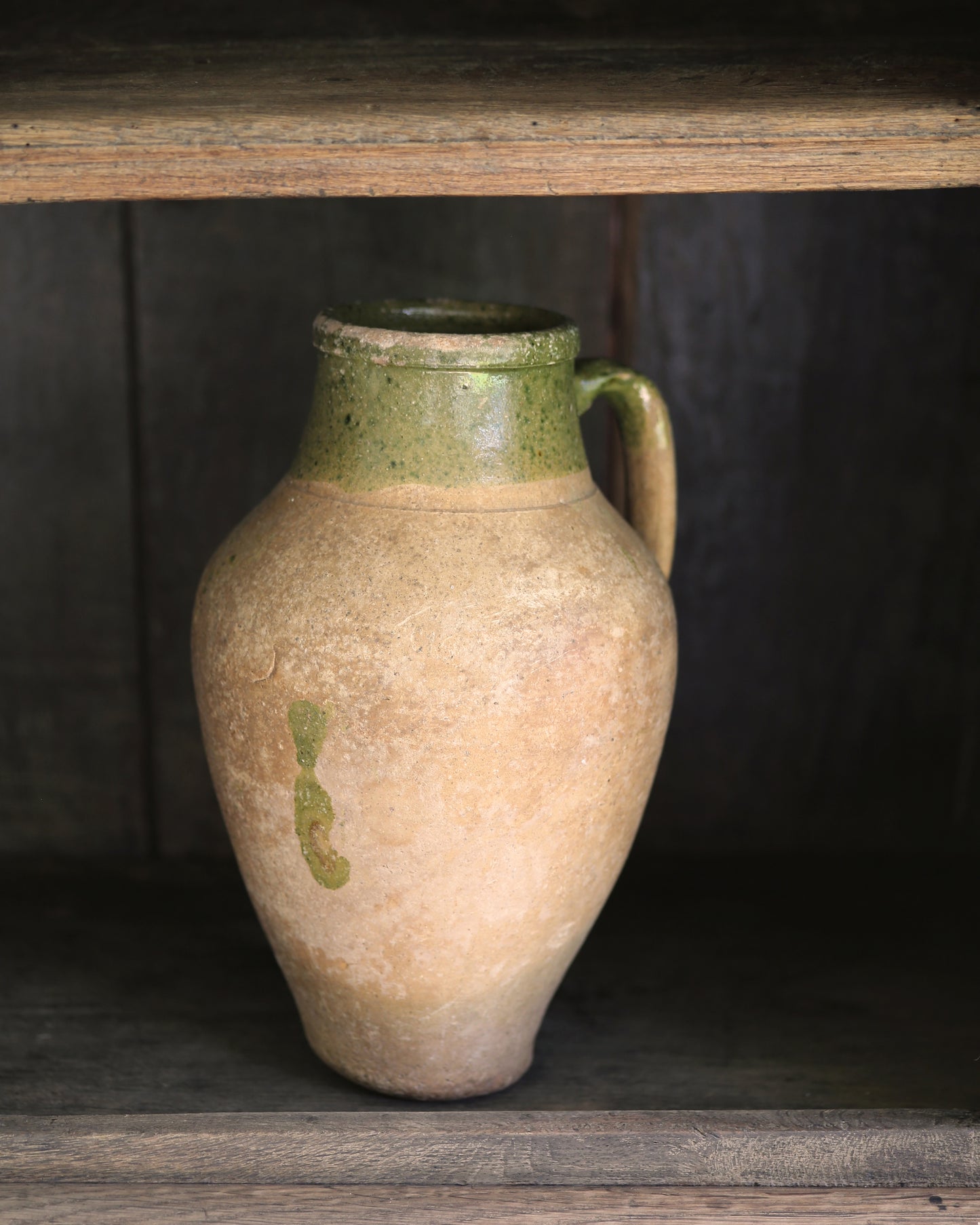 Stoneware pitcher with green rim on a wooden shelf