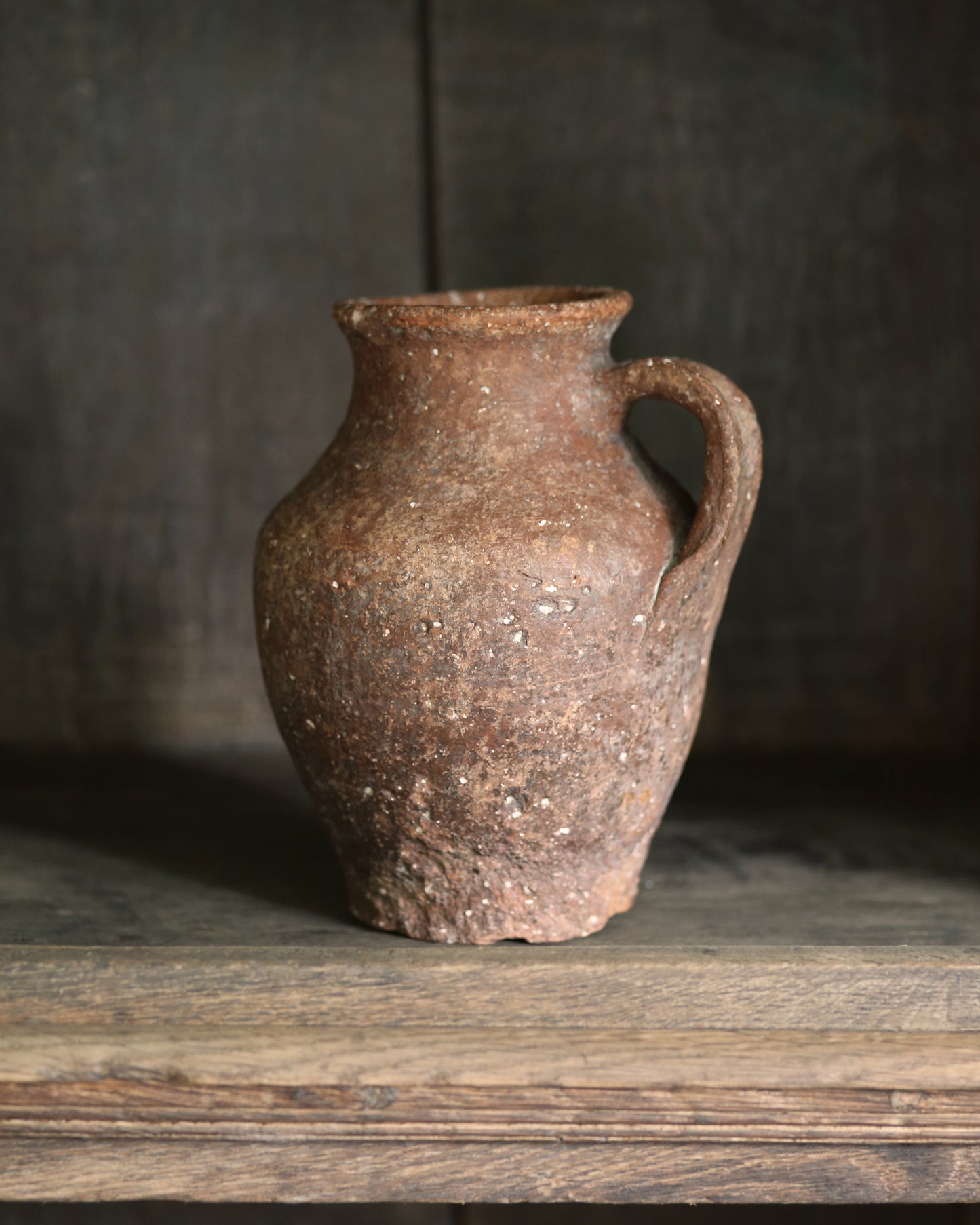 Brown ceramic pitcher pot with lots of rustic texture on a wooden surface with a dark background