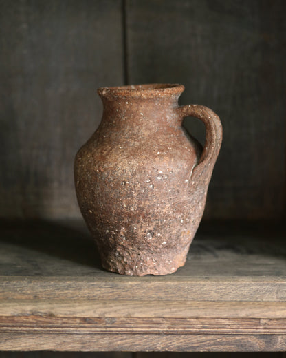 Brown ceramic pitcher pot with lots of rustic texture on a wooden surface with a dark background