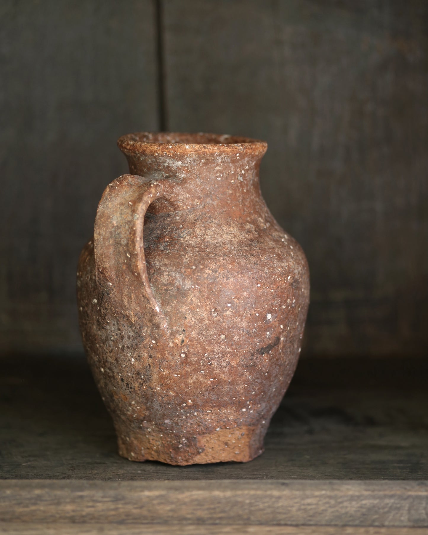 Rustic brown clay vase with a handle on a wooden surface