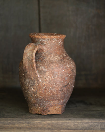 Rustic brown clay vase with a handle on a wooden surface