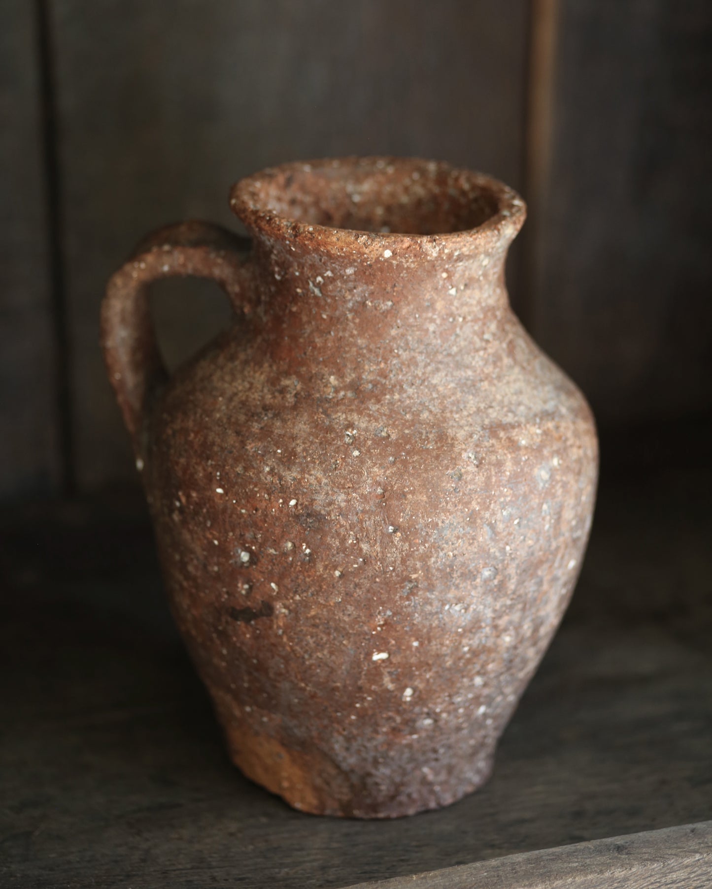 Rustic brown terracotta pottery vase on a dark surface with a blurred background