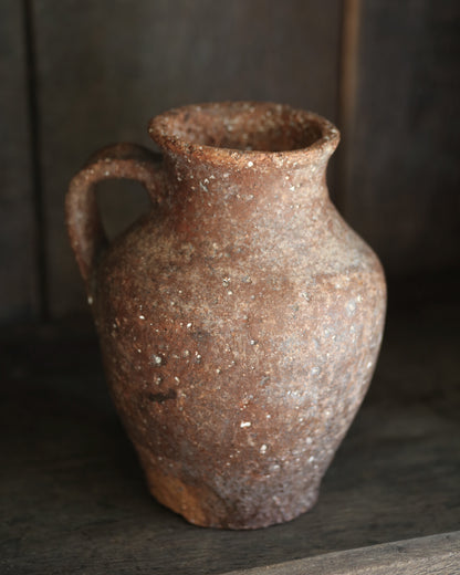 Rustic brown terracotta pottery vase on a dark surface with a blurred background