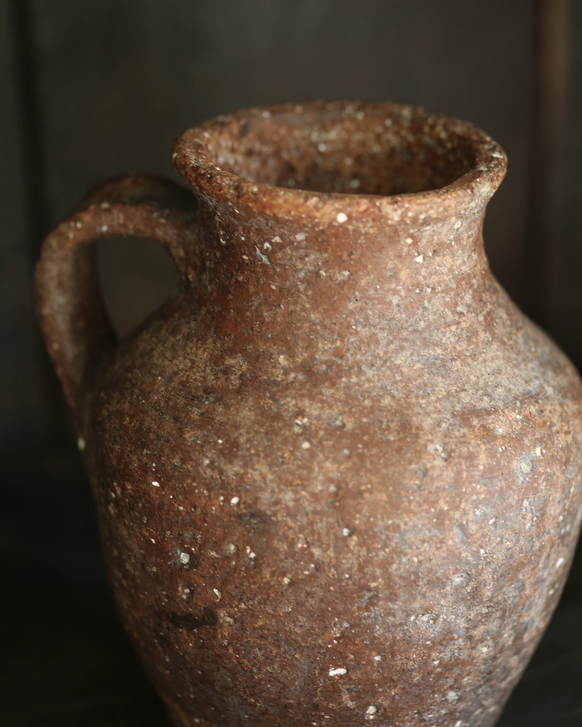Rustic textured antique brown ceramic jar with a handle on a dark background