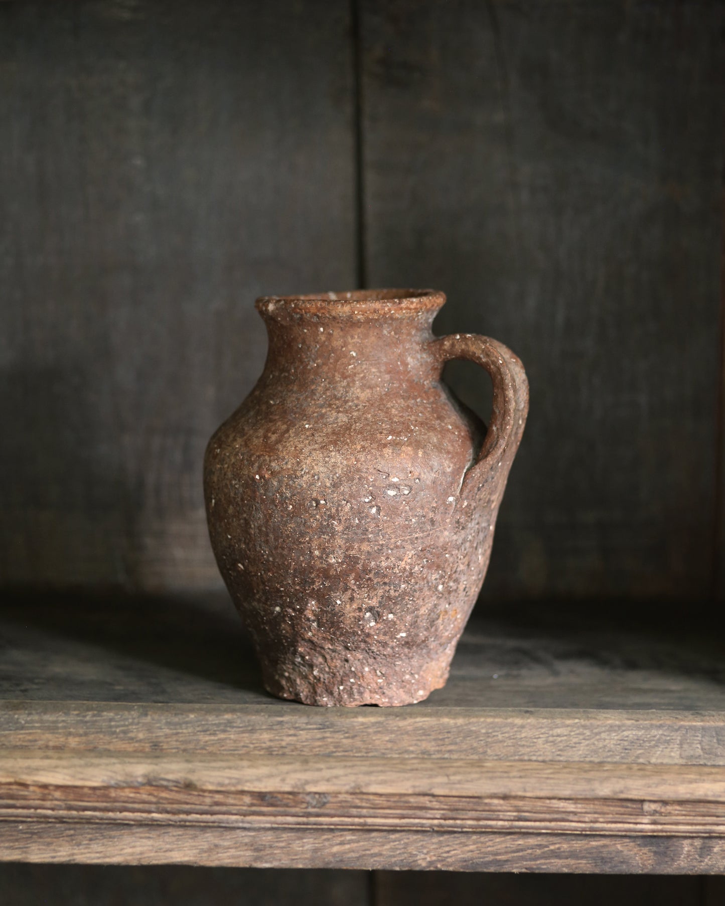 Natural terracotta ceramic pitcher pot on a wooden bookcase