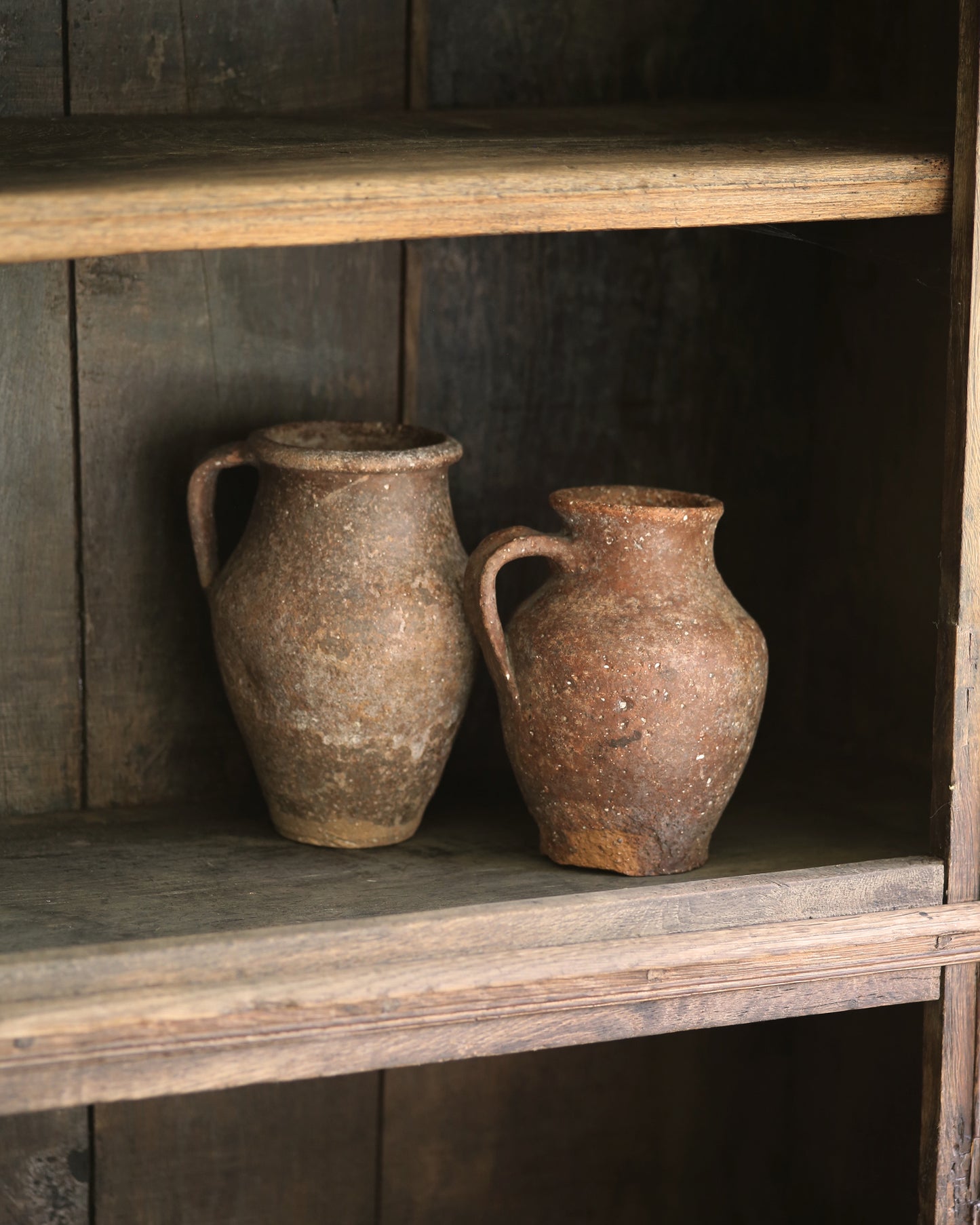 Two rustic antique clay pots styled on an antique wooden bookcase.