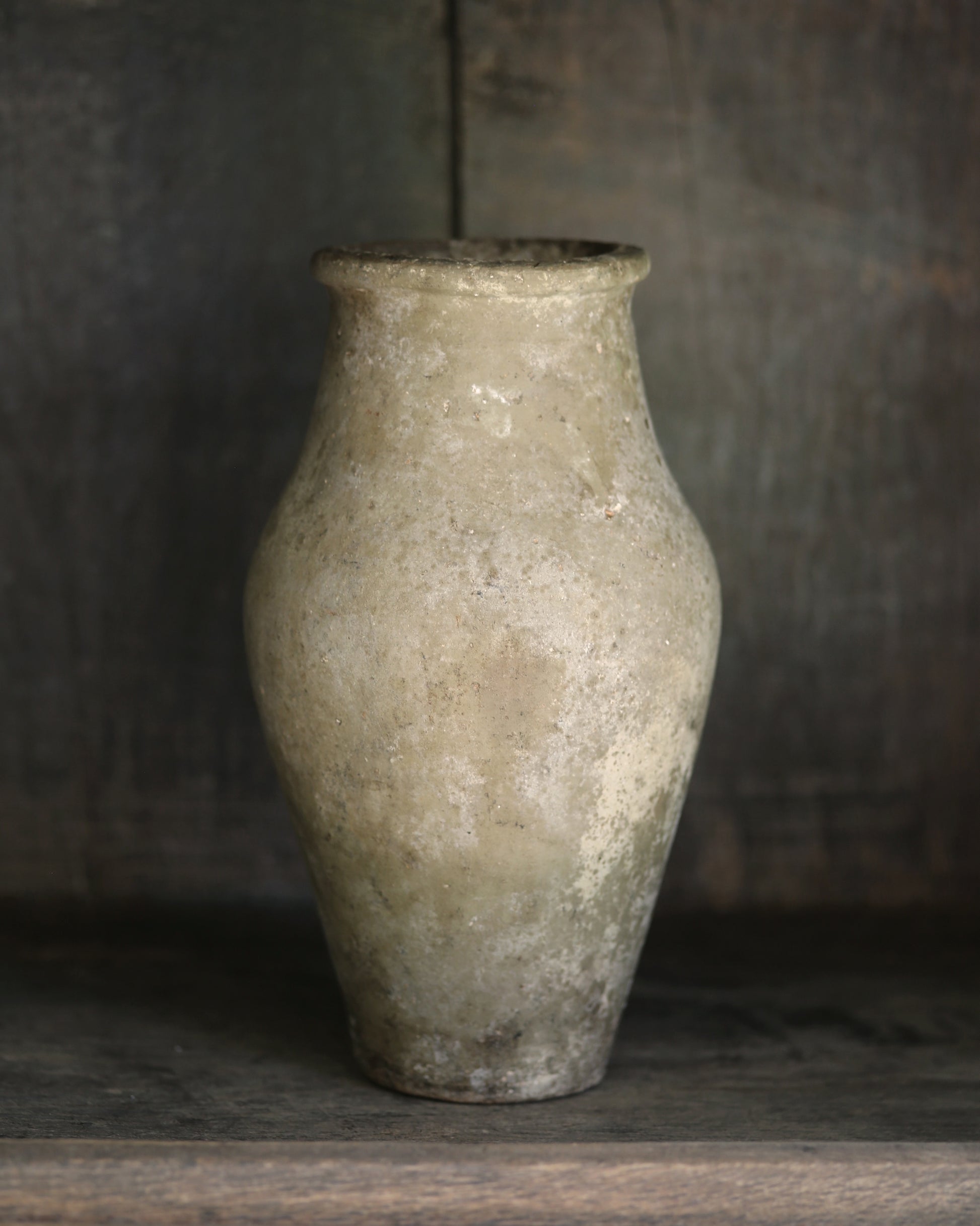 Antique clay vase in pale neutral tones on a wooden shelf