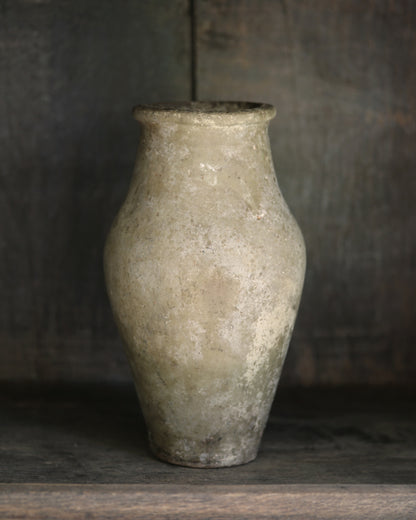 Antique clay vase in pale neutral tones on a wooden shelf