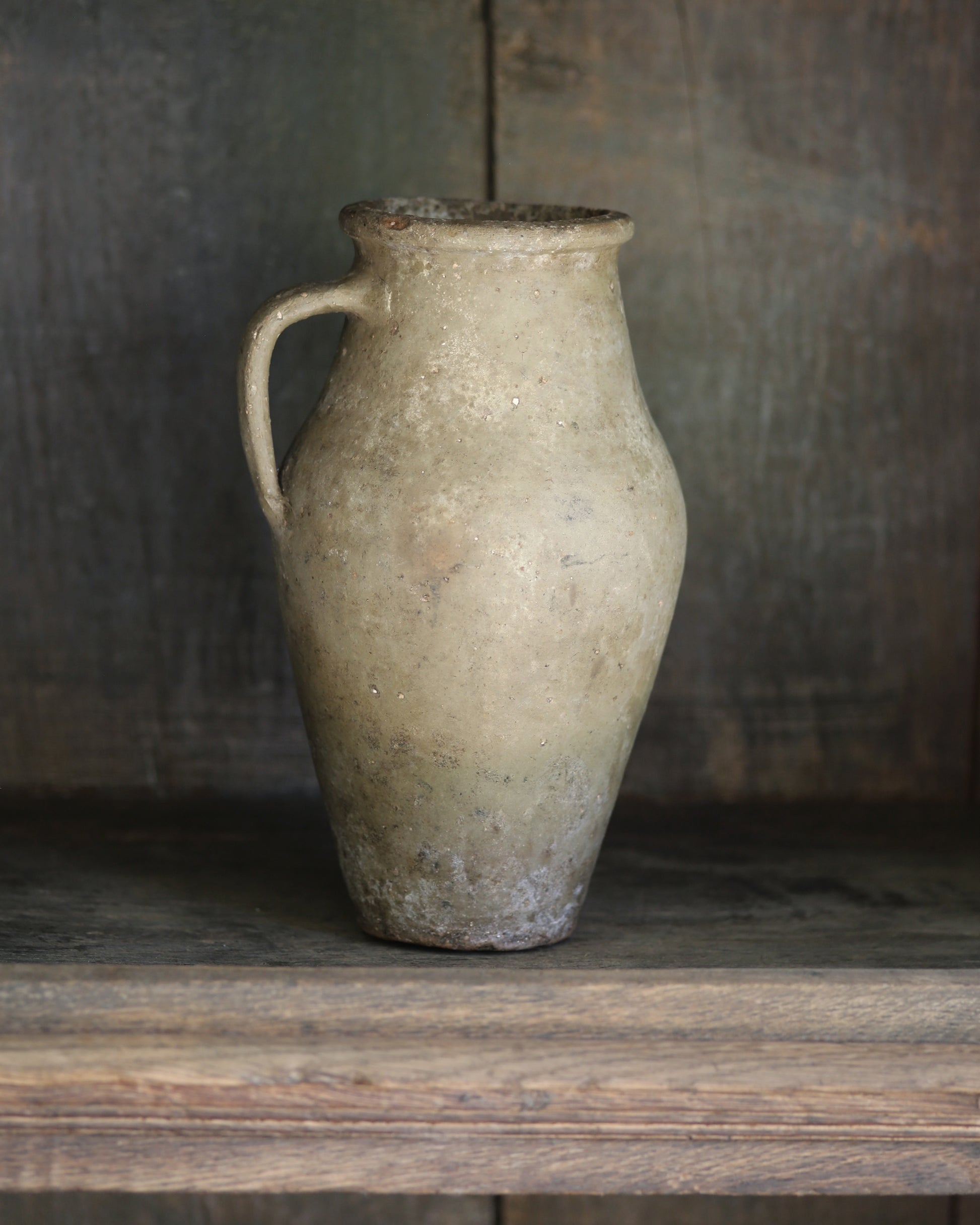 Rustic clay pitcher vase on a dark wooden bookcase shelf