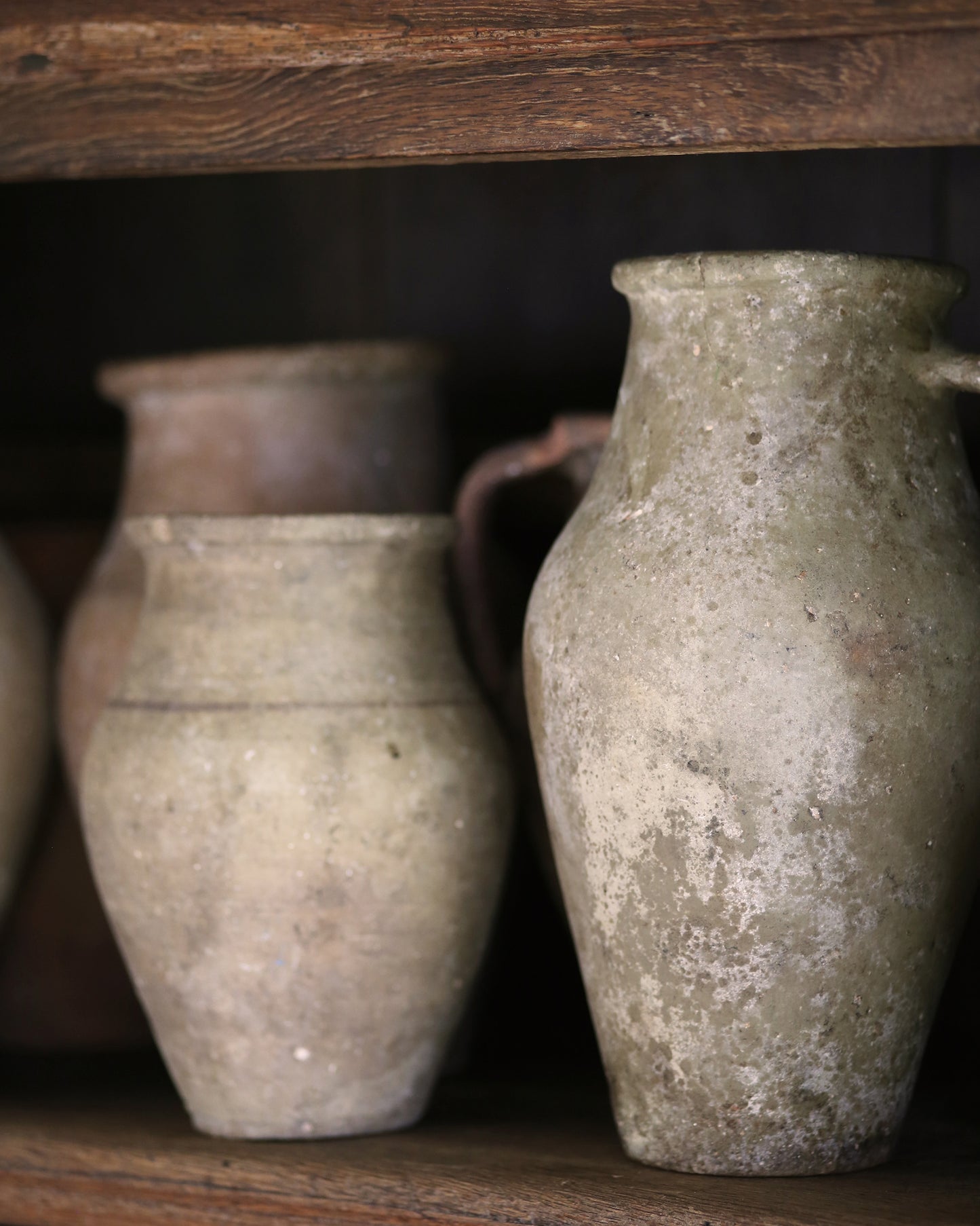 Two ancient clay pots on a wooden shelf in a bookcase